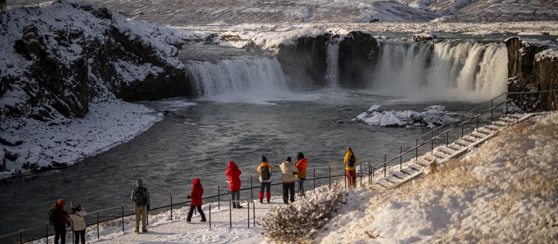 Iceland cruising: visitors view a snow-covered waterfall from a fenced path | Jacques Marais