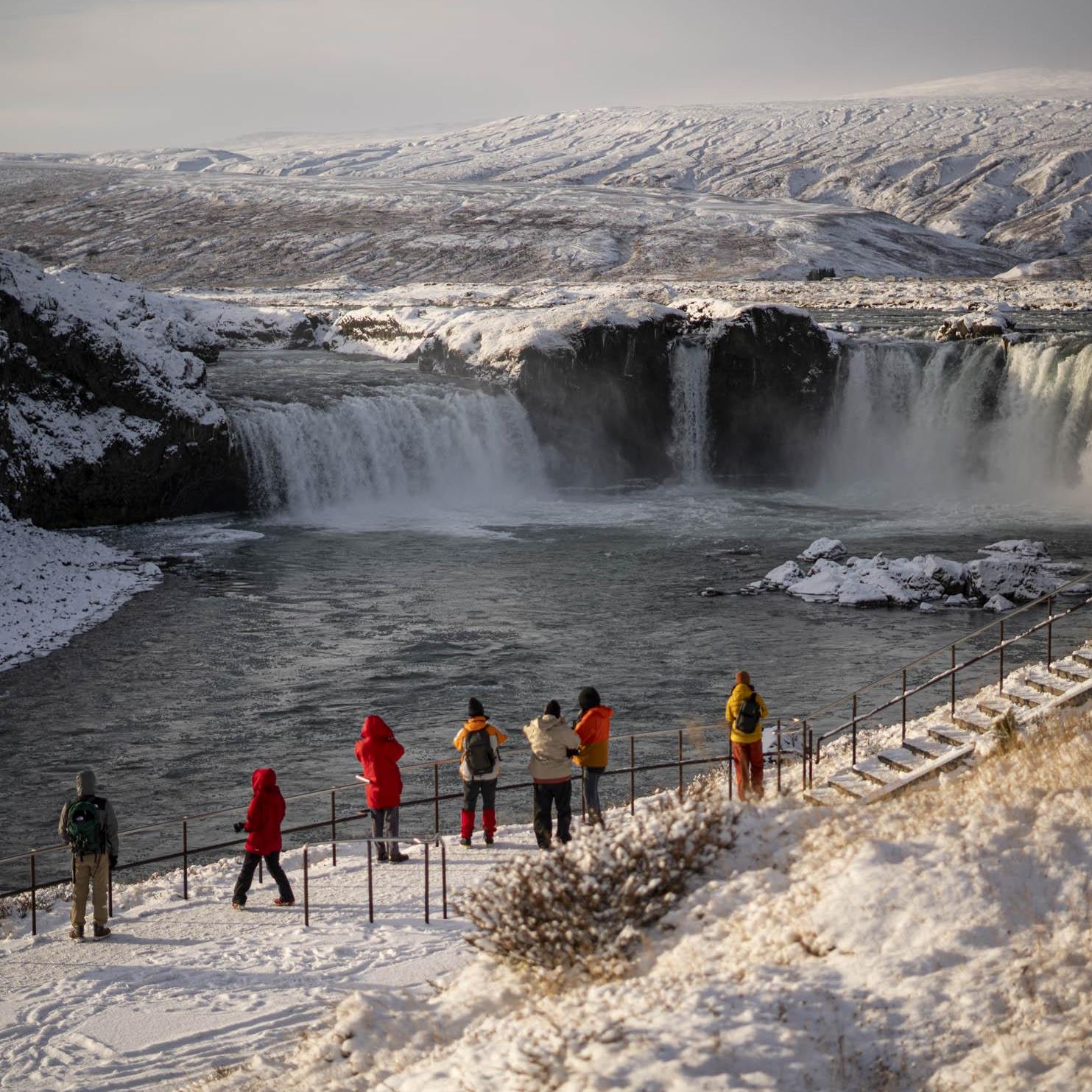 Iceland cruising: visitors view a snow-covered waterfall from a fenced path | Jacques Marais