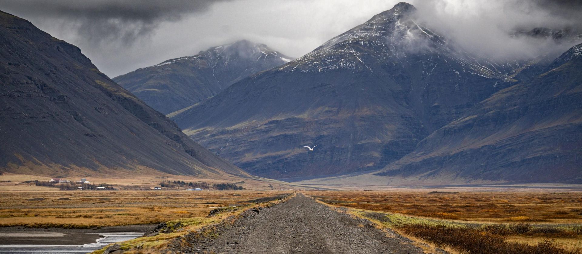 Iceland gravel road crossing a valley toward snow capped peaks | Jacques Marais