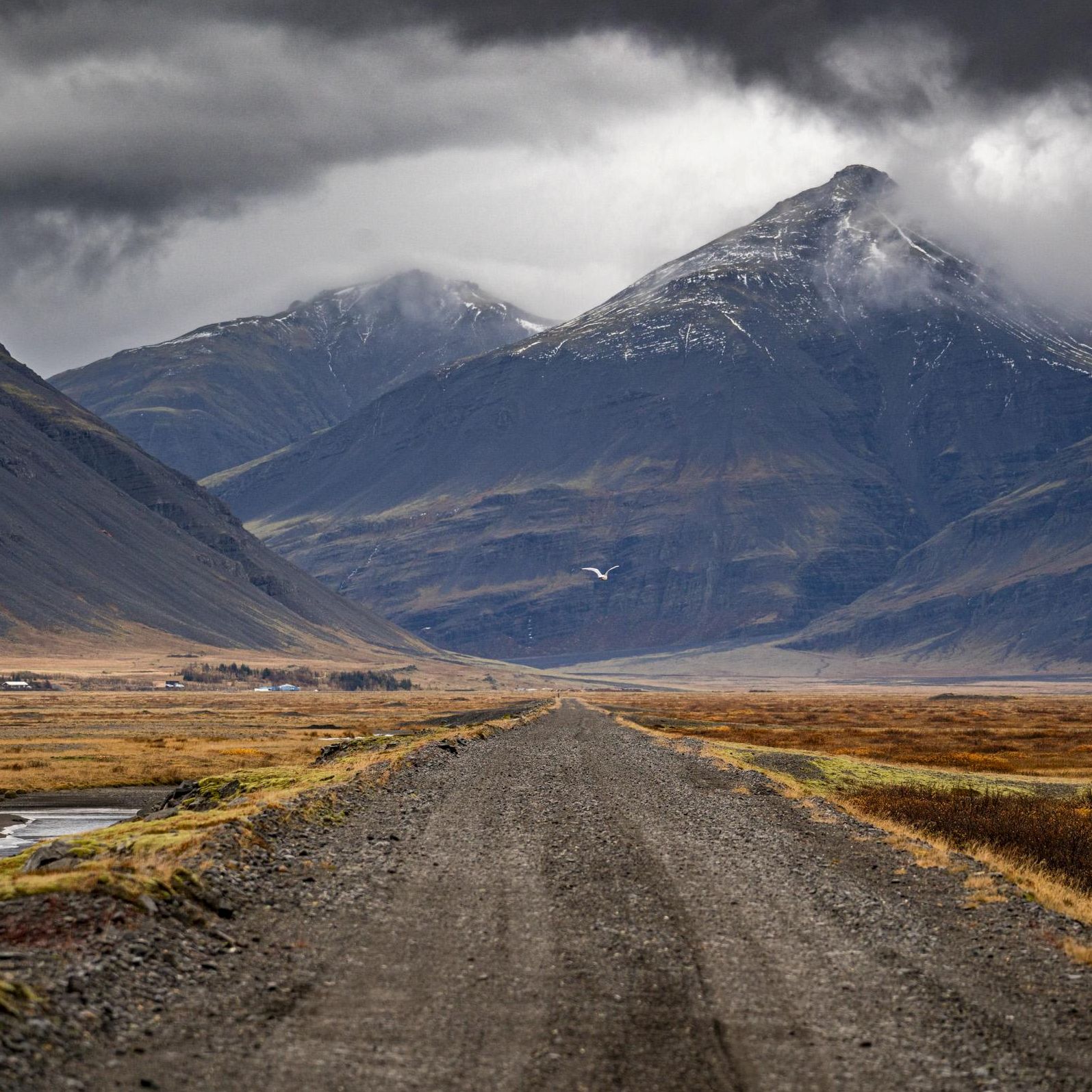 Iceland gravel road crossing a valley toward snow capped peaks | Jacques Marais